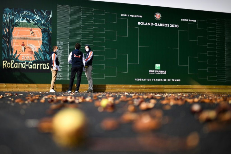 Members of staff speak in front of a scoreboard as autumn chestnuts litter the grounds of Roland Garros