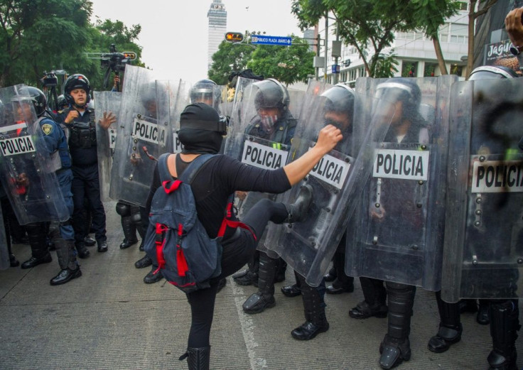 A woman kicks a policeman's shield in Mexico City during a September 26, 2020 demo marking the sixth anniversary of the disappearance of 43 students in the city of Iguala, Guerrero