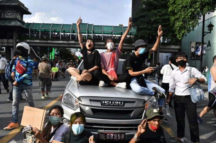 Protesters give the three-finger salute while sitting on a police vehicle