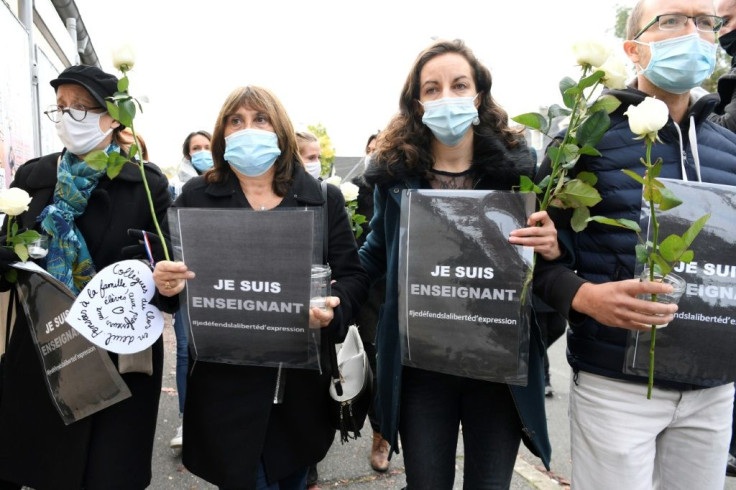 People hold a sign reading 'I am a teacher - Freedom of speech' outside the school where Paty worked