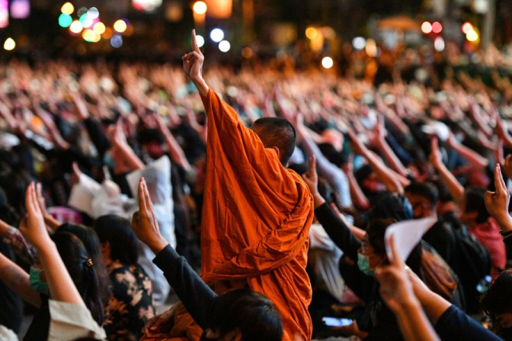 A Buddhist monk gives the three-finger salute with pro-democracy protesters during a rally at Asok in Bangkok