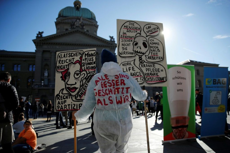 A healthcare worker wears a PPE suit reading in German "All are better protected than we are!" outside the Swiss House of Parliament during a demonstration in Bern