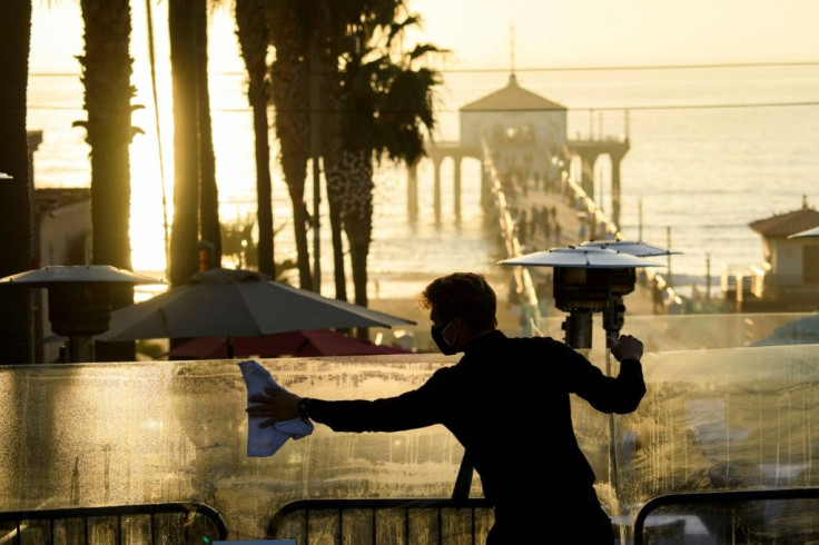 A restaurant employee cleans a plexiglass table divider while preparing for outdoor dining service in Manhattan Beach, California, a few hours before the start of the new 10:00 pm to 5:00 am curfew