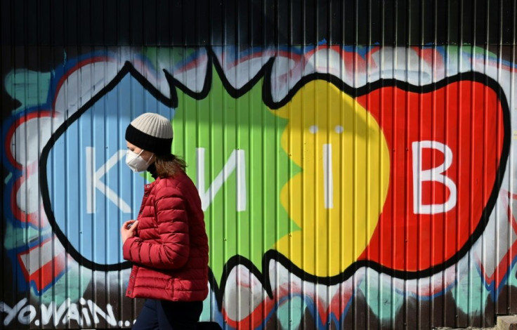 A woman wearing a protective face mask walks in front of a graffiti reading "Kiev" during a warm spring day in the Ukrainian capital on April 1, 2021, amid the ongoing coronavirus disease pandemic