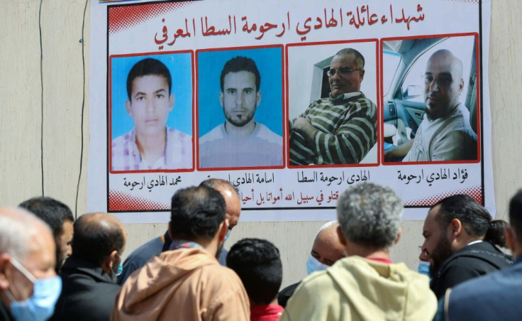 Libyans gather by a wall poster depicting victims from one family during a funeral procession for 12 bodies that were identified from mass graves found in Tarhuna town