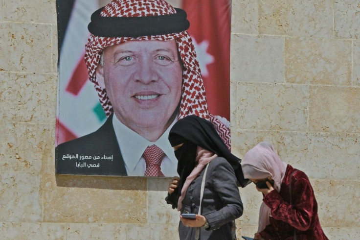 Women walk past a poster of Jordan's King Abdullah II on a street in the capital Amman on Tuesday