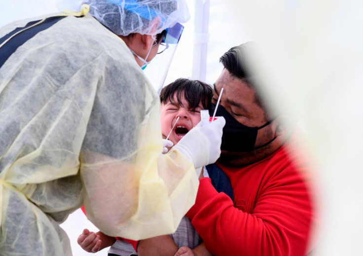 Jose Vatres (R) holds his son Aidin who reacts as nurse practitioner Alexander Panis (L) takes a nasal swab sample to test for COVID-19 at a mobile testing station in a public school parking area in Compton, California, just south of Los Angeles, on April