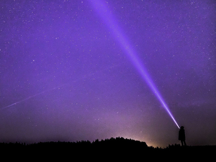Representation. A woman looks up at the night sky while a light shines.
