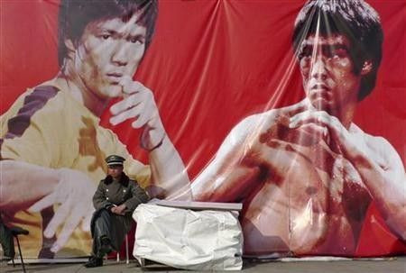 A security guard sits in front of an advertising poster of martial arts movie star Bruce Lee at the Olympic Park in Beijing, Nov. 4, 2009.