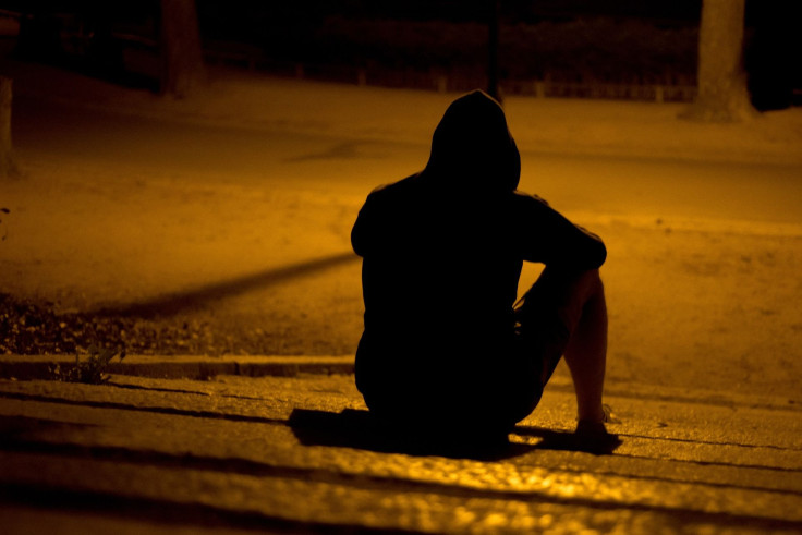 Representation. A hooded person sitting by the road.
