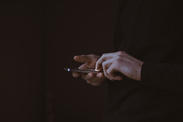 Representation. A person typing on a phone in a dark room.