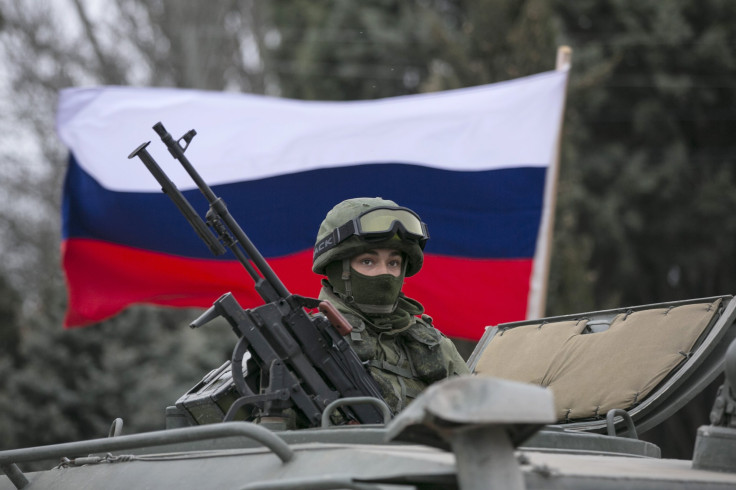 A pro-Russian man (not seen) holds a Russian flag behind an armed servicemen on top of a Russian army vehicle outside a Ukrainian border guard post in the Crimean town of Balaclava March 1, 2014. Ukraine accused Russia on Saturday of sending thousands of