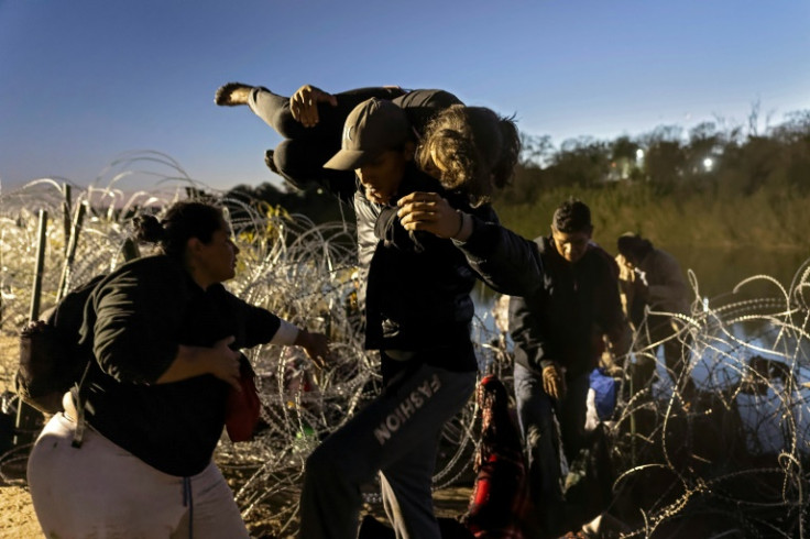 Migrants pick their way through razor wire as they seek to enter the United States across a border that has seen an unprecedented influx