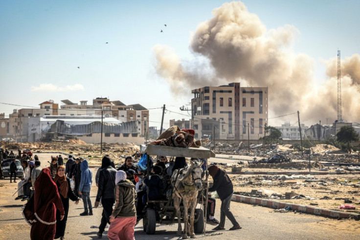 Smoke from bombardment billows in the background as displaced Palestinians flee Khan Yunis