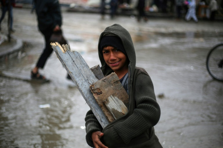 A youth gathers wood in rainy weather at a makeshift tent camp in Rafah