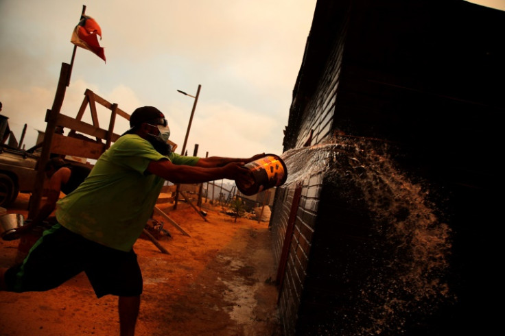 A man douses a burned building with water in Quilpe, where wildfires blazed through the night