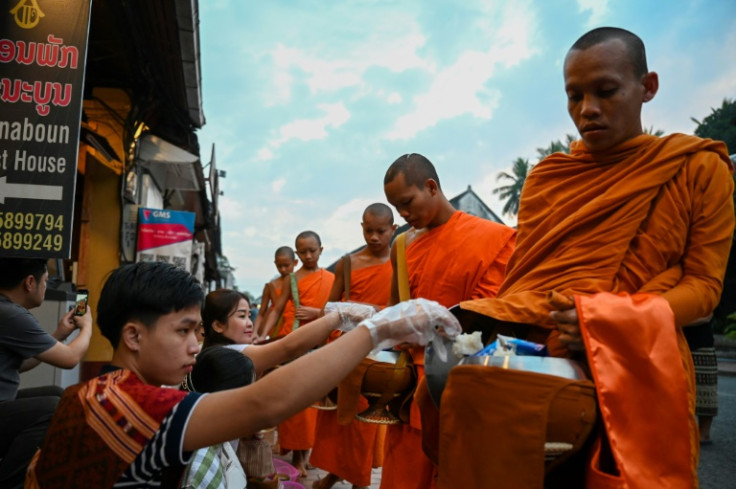 Monks have to make their way through hundreds of visitors on plastic stools offering alms as tour guides thrust mobile phones into their faces