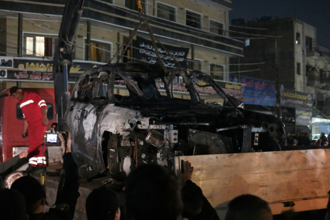 People watch as a vehicle that was hit by a deadly drone strike is removed from a Baghdad neighbourhood