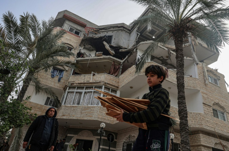 A young Palestinian carries wood past a destroyed residential buidling in Rafah