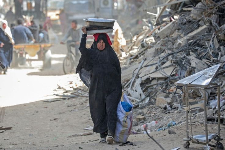 A displaced Palestinian woman carries her belongings through a street amid the rubble of houses destroyed by Israeli bombardment in Khan Yunis in the southern Gaza Strip