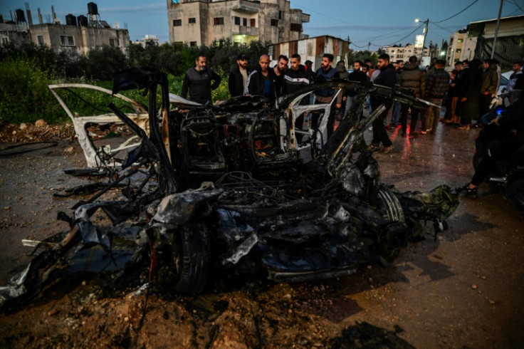 Palestinian men surround a charred car hit in an Israeli air strike on Jenin