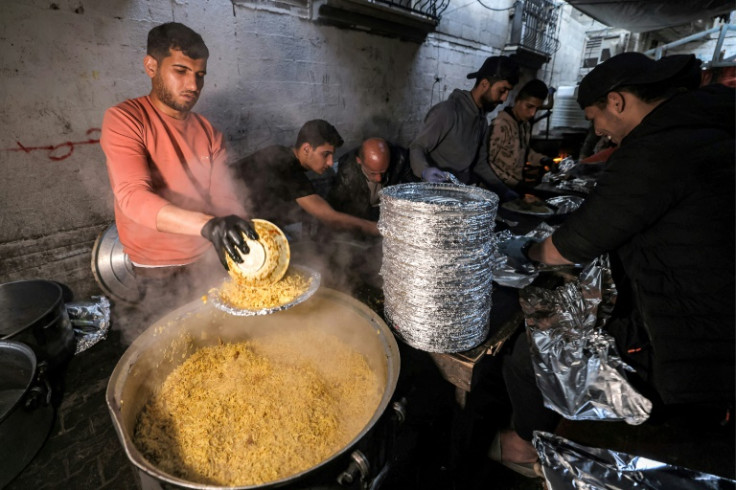 Volunteers serve meals for people breaking their fast during the holy month of Ramadan in a refugee camp in Rafah in the southern Gaza Strip on March 24, 2024