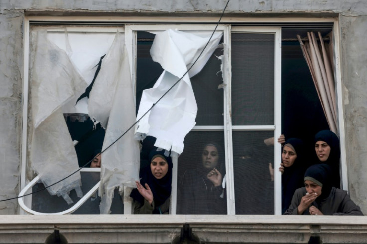 Palestinian women watch from a damaged apartment as dead relatives are transferred into a vehicle following overnight bombardment in Rafah in the southern Gaza Strip, on April 2, 2024