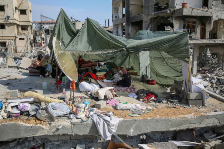 Palestinians shelter in a makeshift tent made from a parachute used to airdrop food aid, set up on the rubble of their home in a devastated area around Gaza's Al-Shifa hospital on April 2, 2024