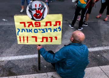 A man sits with an anti-Netanyahu sign during a demonstration in Tel Aviv