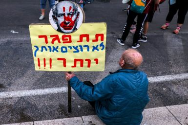 A man sits with an anti-Netanyahu sign during a demonstration in Tel Aviv