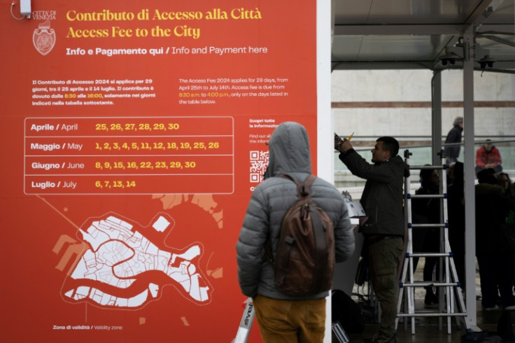 A person reads an information board as workers setup a control booth near Santa Lucia train station on April 24, 2024 in Venice