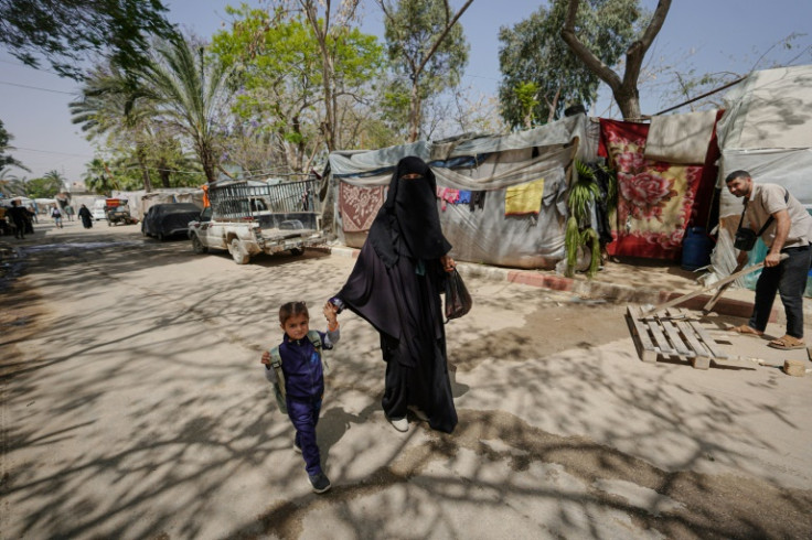 A displaced Palestinian woman holds a child by the hand as she walks in front of tents set up inside the European hospital compound in Khan Yunis in the southern Gaza Strip