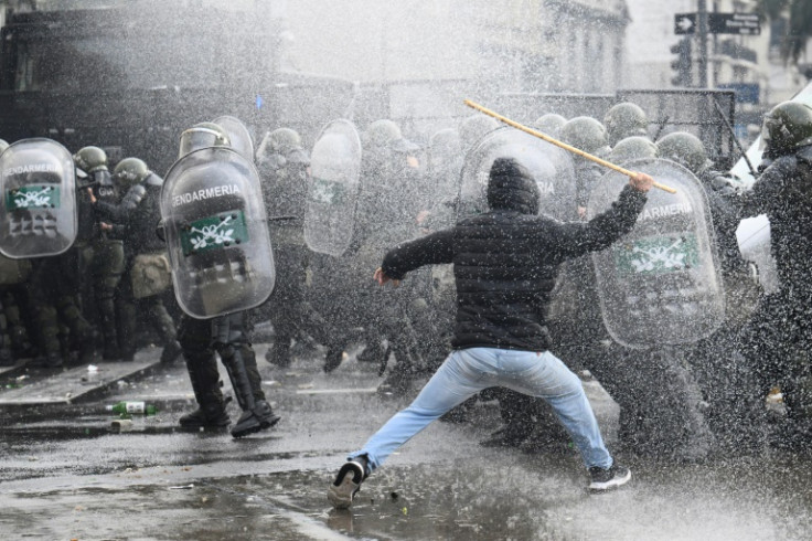 A demonstrator clashes with riot police while being sprayed from a police water cannon outside the National Congress in Buenos Aires