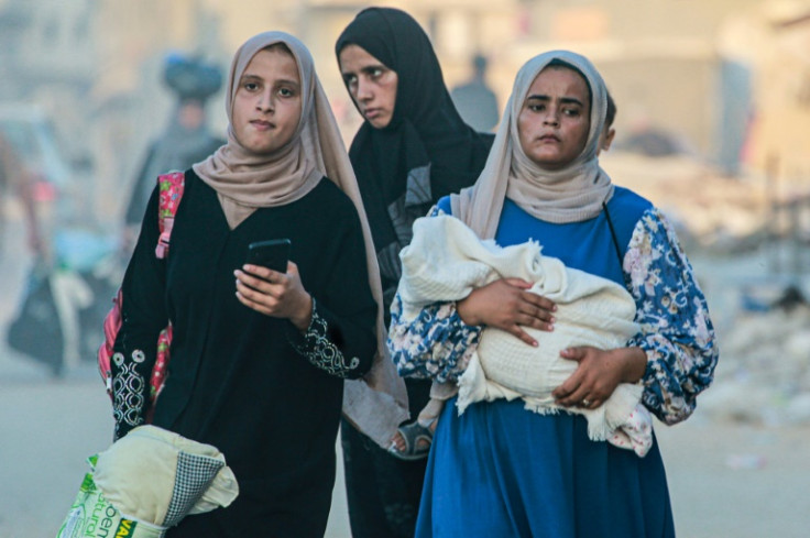 A displaced Palestinian woman holds a baby wrapped in a blanket
