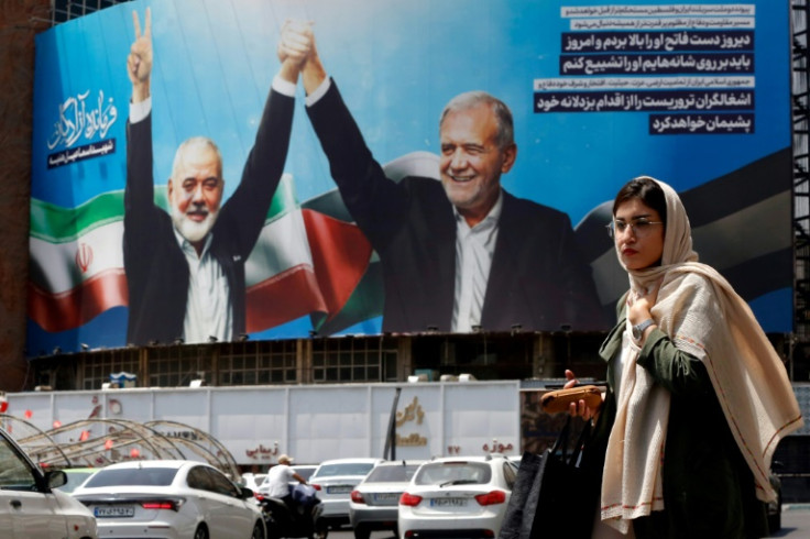 A woman walks past a picture of Iranian President Masoud Pezeshkian (R) and slain Hamas leader Ismail Haniyeh in Tehran