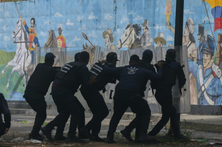 Police officers take cover from demonstrators during an anti-Maduro protest in Caracas on July 29, 2024
