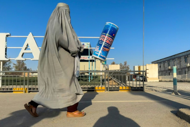 An Afghan burqa-clad woman walks past an energy drink advertisement in Kandahar