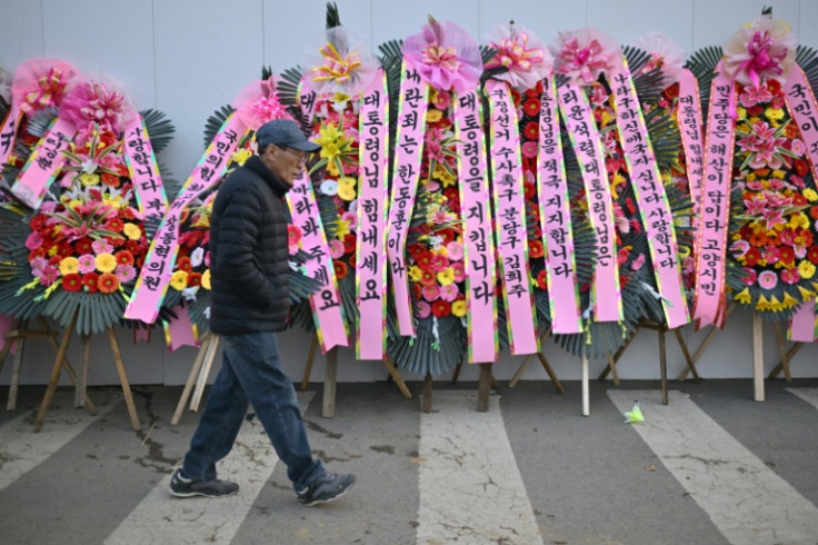 A man walks past flowers displayed in support of South Korea President Yoon Suk Yeol outside the Presidential Office