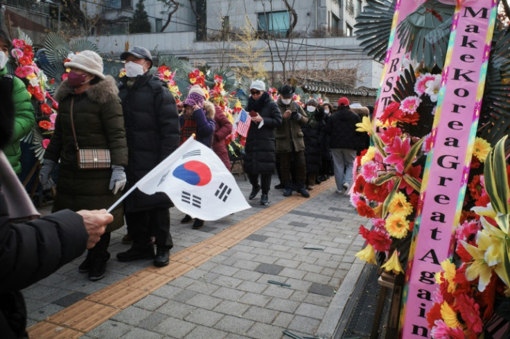 Supporters of impeached South Korean president Yoon Suk Yeol queue up for food beyond flowers outside his home