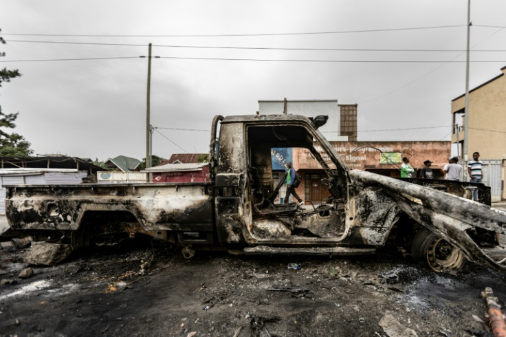 Residents walk past the wreckage of a burned vehicle in Goma
