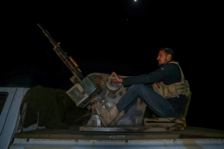 A member of the Syrian security forces mans a gun in the back of a pickup truck as they prepare to depart from Al Mastumah, Idilib province