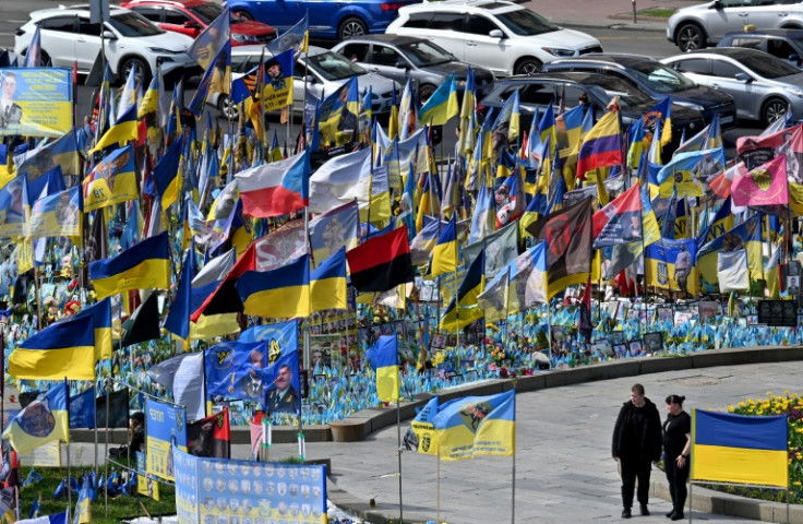 A couple walks by flags and portraits of fallen servicemen at a makeshift memorial for the fallen Ukrainian and foreign fighters, at the Independence Square in Kyiv on April 19, 2025