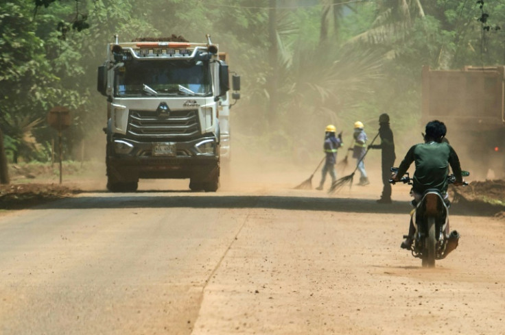 Workers armed with brooms, goggles, hats and scarves sweep an access road that carries 6,000 tonnes of ore destined for China each day