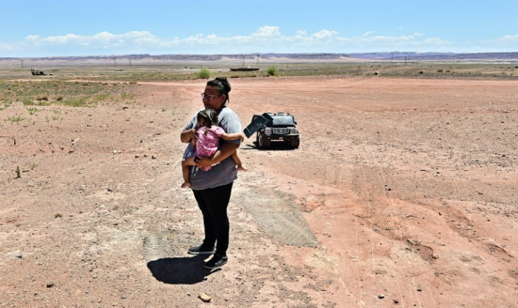 Navajo Nation resident Gilberta Cortes, 42, who uses a generator for electricity, carries her child outside her home in Cameron, Arizona on July 9, 2025, as she waits for electricity from the power grid to reach her residence