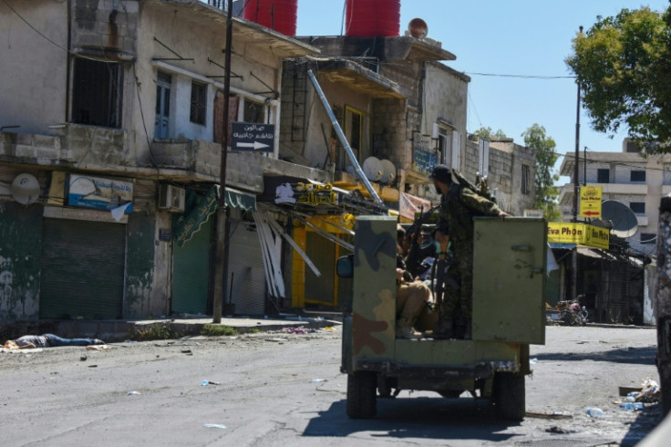 A Syrian government patrol passes a body on the roadside on Wednesday during the army's brief deployment in Sweida.