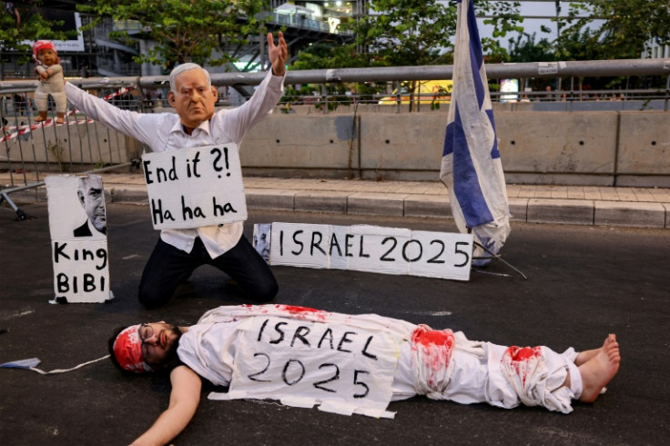 A demonstrator wearing a mask depicting Israeli Prime Minister Benjamin Netanyahu with an elongated nose, evoking the literary character Pinocchio, poses above another lying on the ground while depicting an Israeli hostage during an anti-government protes
