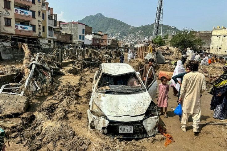 People gather near a damaged vehicle and debris after flash flooding wiped out a road in monsoon-hit northern Pakistan